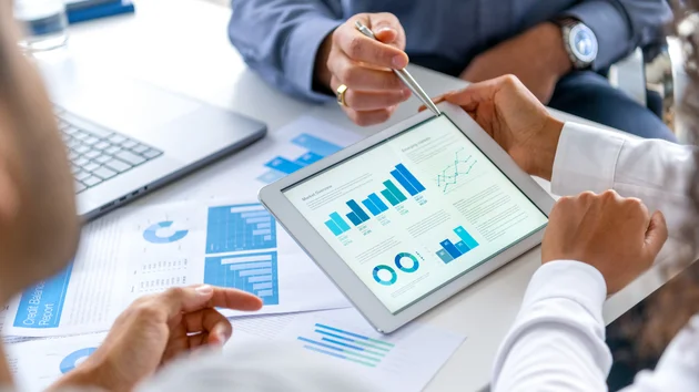 Close up of three people looking at financial data with graphs and charts.