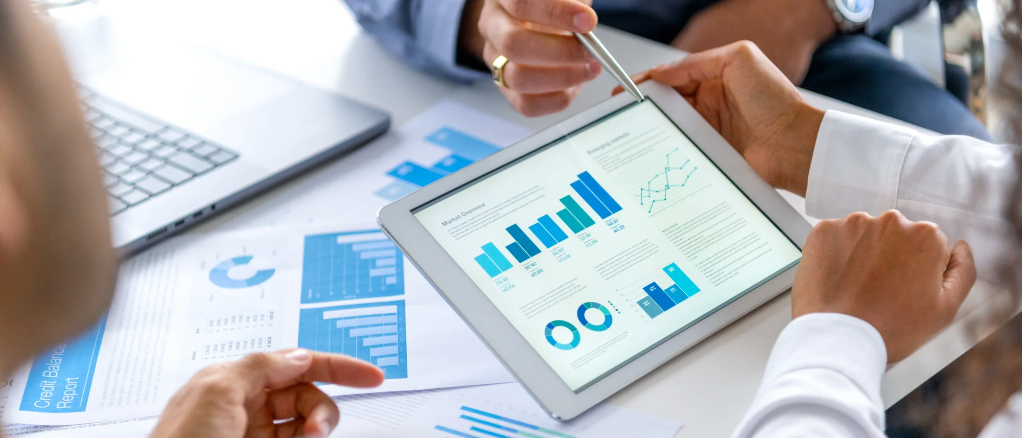 Close up of three people looking at financial data with graphs and charts.